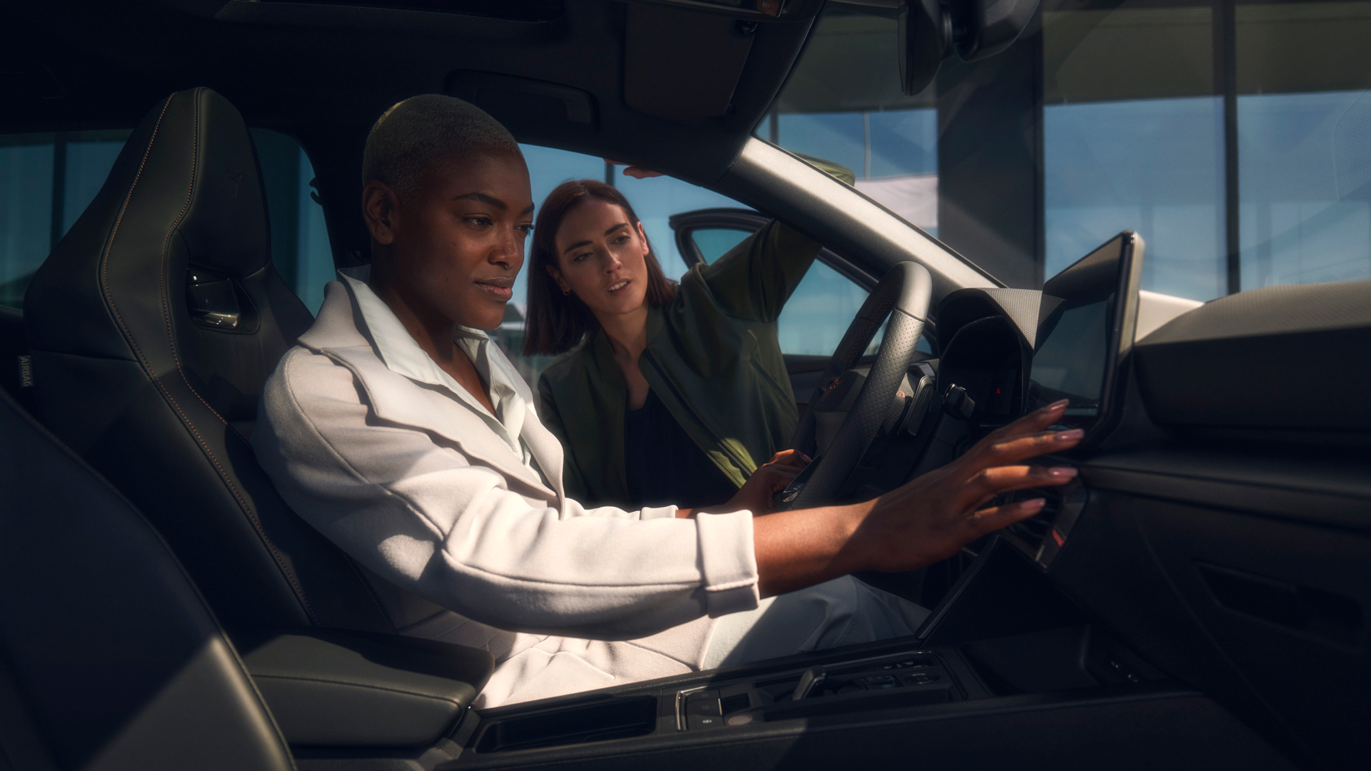 Zwei Personen im CUPRA Innenraum eine Person greift zum Infotainment Display